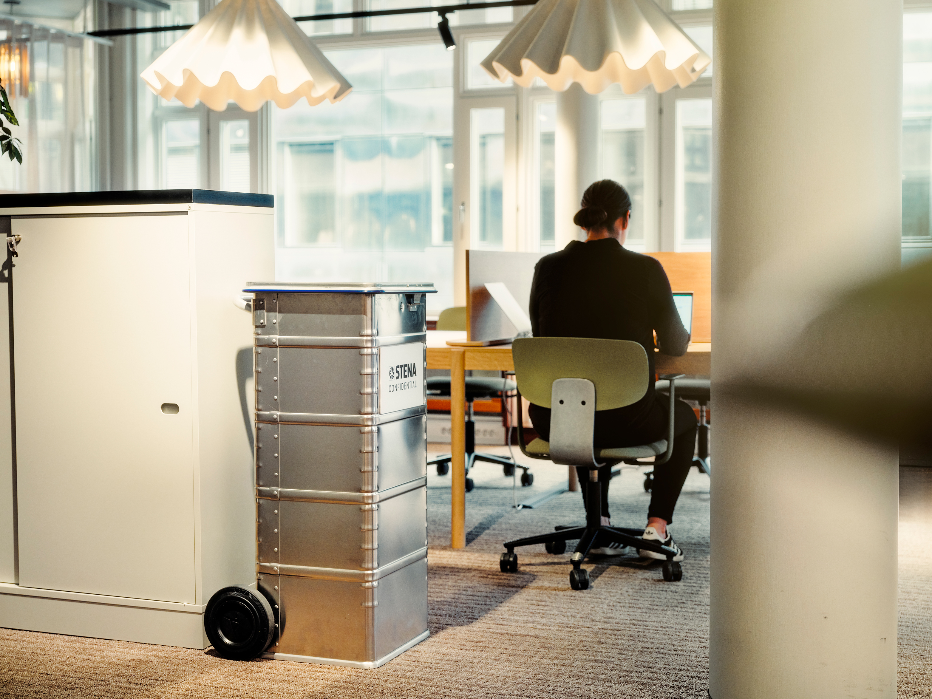 Nainen istuu pöydän ääressä selkä kameraan päin.