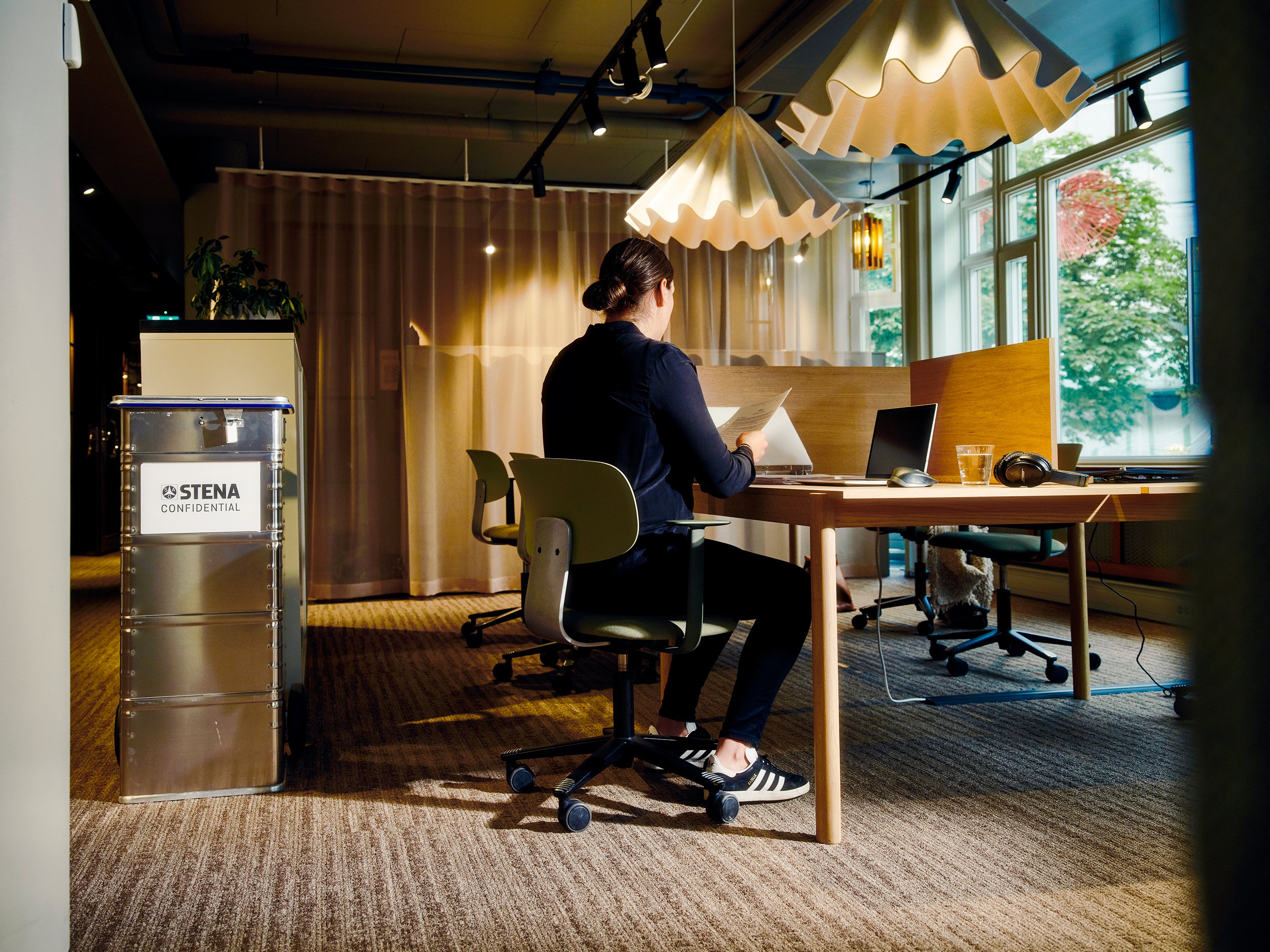 Kvinna sitter vid ett skrivbord bredvid ett Stena Confidential kärl.