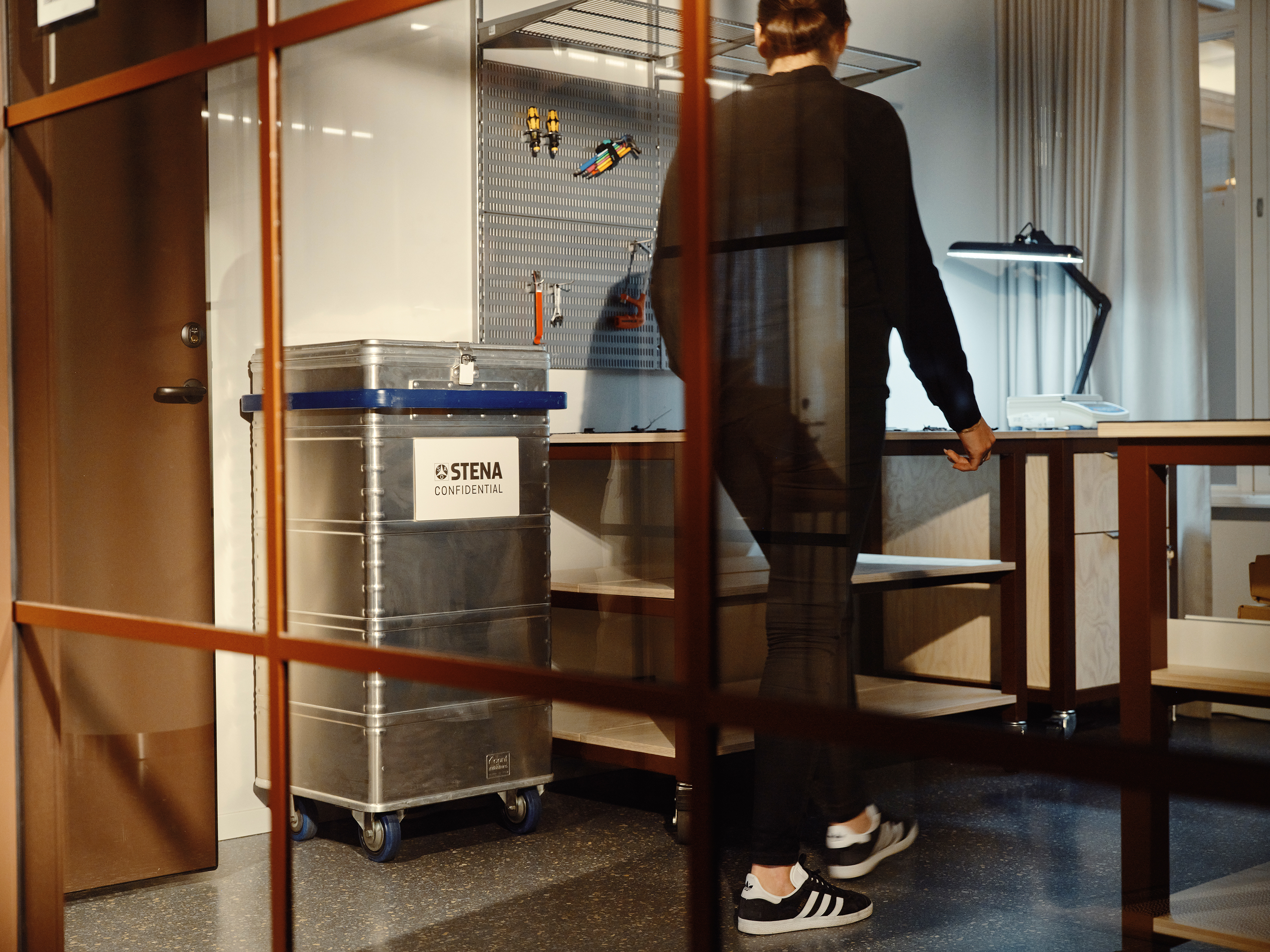 Henkilö kävelee toimistossa tietoturva-astian vierestä